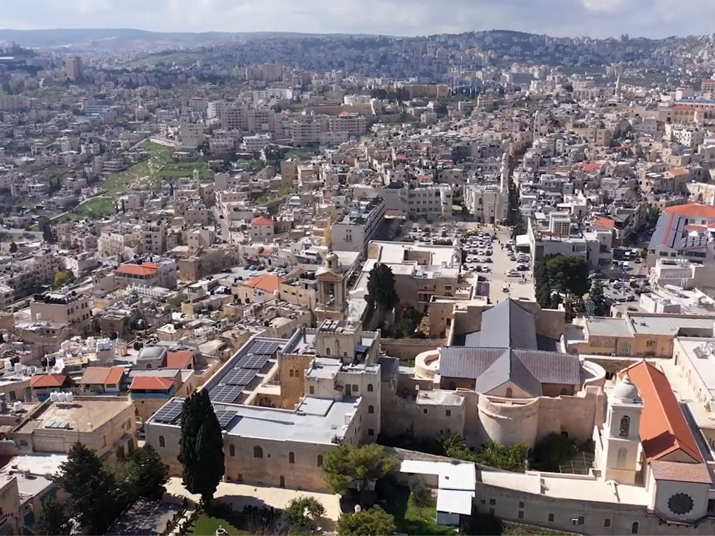 Aerial view of a city in Israel with short white buildings across the landscape opening to a mountain in the distance.