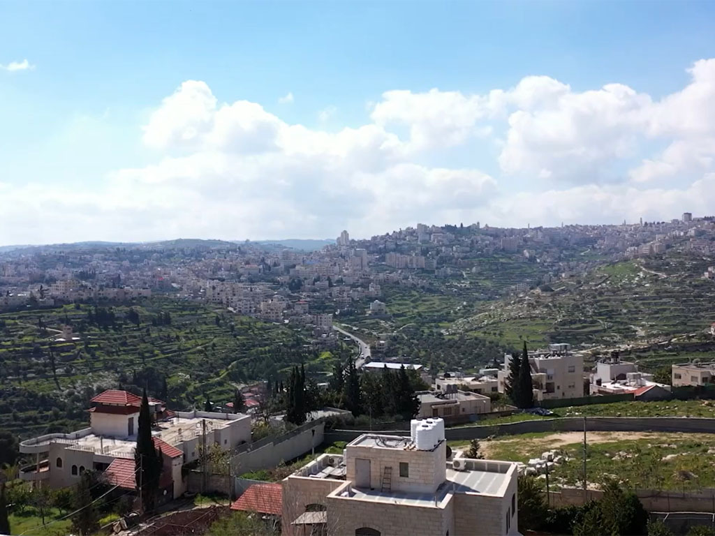 Aerial view of a city in the Holy Land built up on a hill in the distance. 