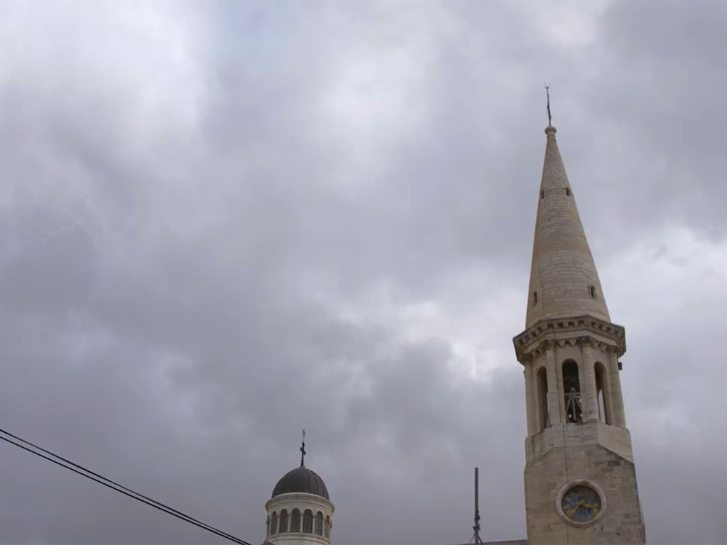 A gray stone steeple rises against a dark clody sky.