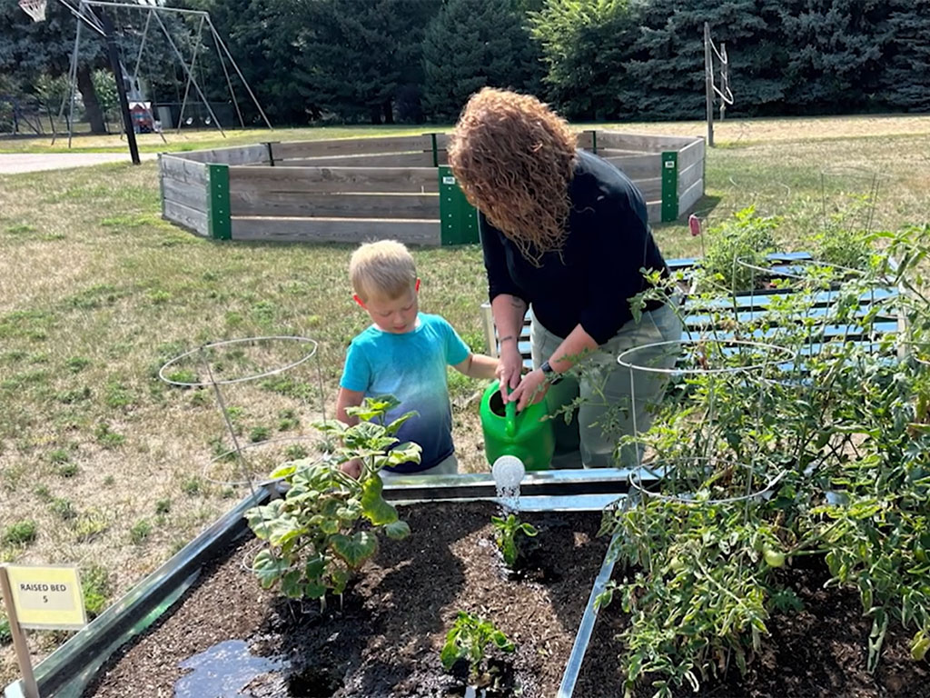 Adult and young child watering plants together in a garden bed