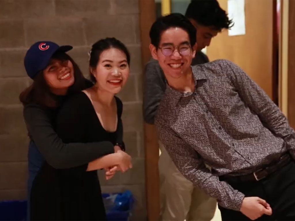 Three young adults smile for the camera – one female in a Cubs hat holds another female while a male leans into the picture.