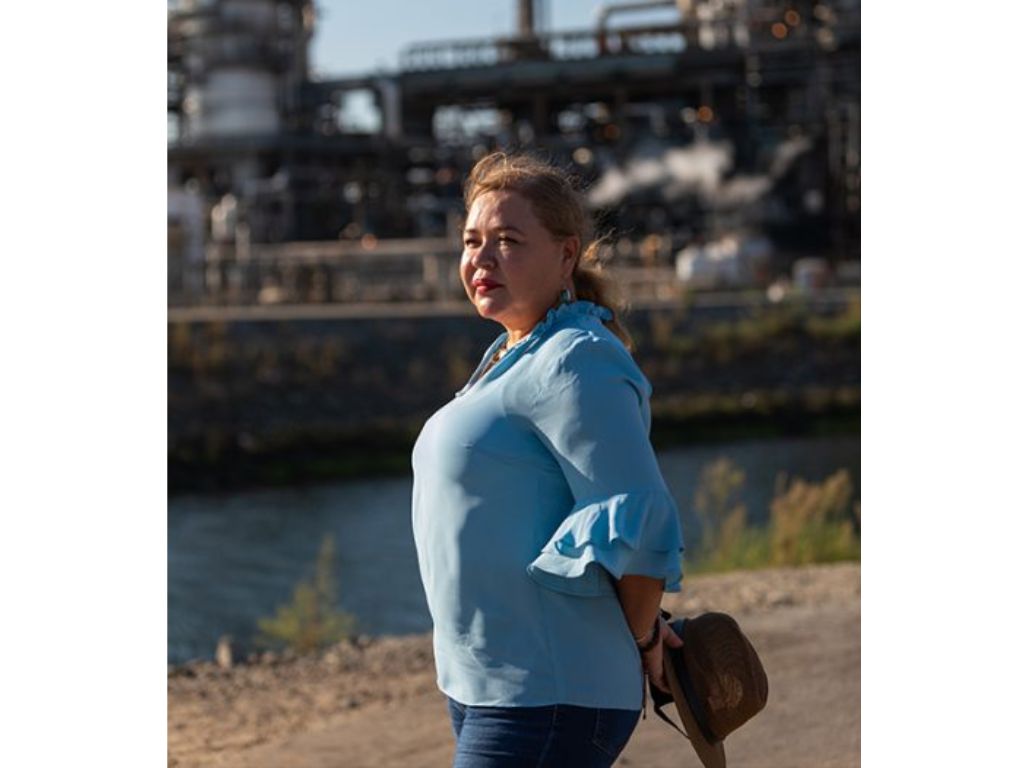 A woman in a blue long-sleeve shirt stands alone looking off to her left.