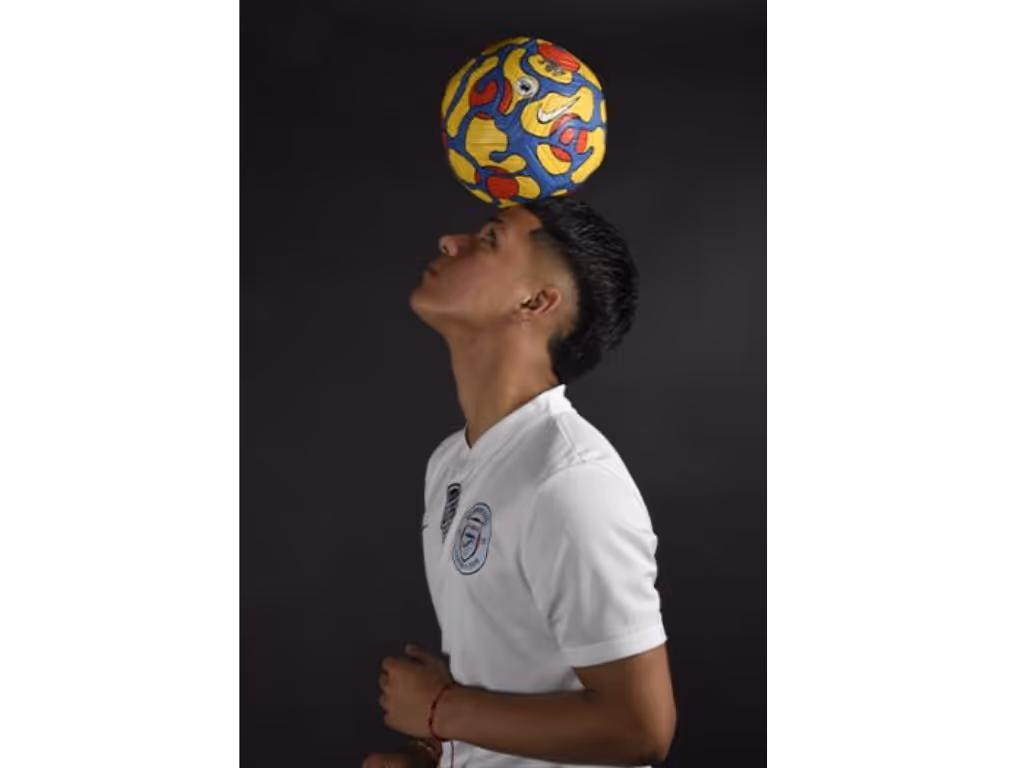 Teenage male balancing a soccer ball on his head.