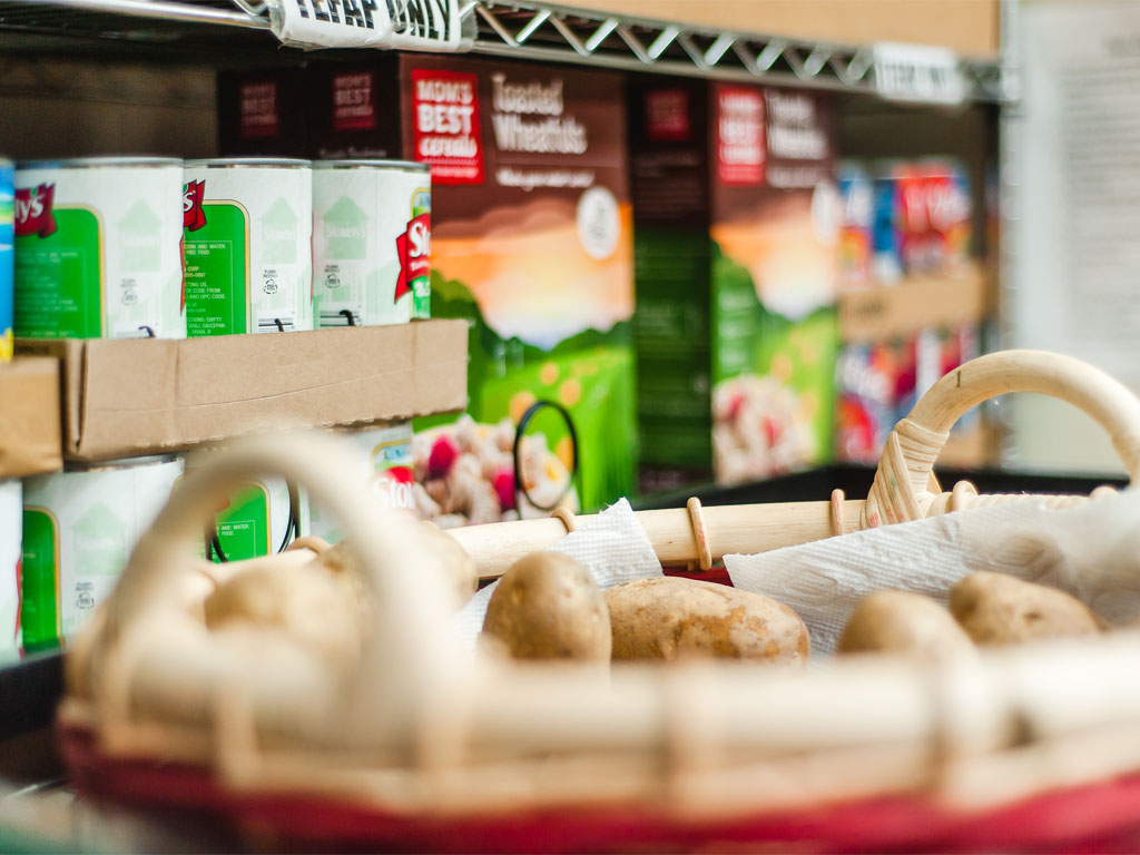 close-up of a basket of potatoes sitting in front of a shelf with food cans and boxes in a food prantry. 