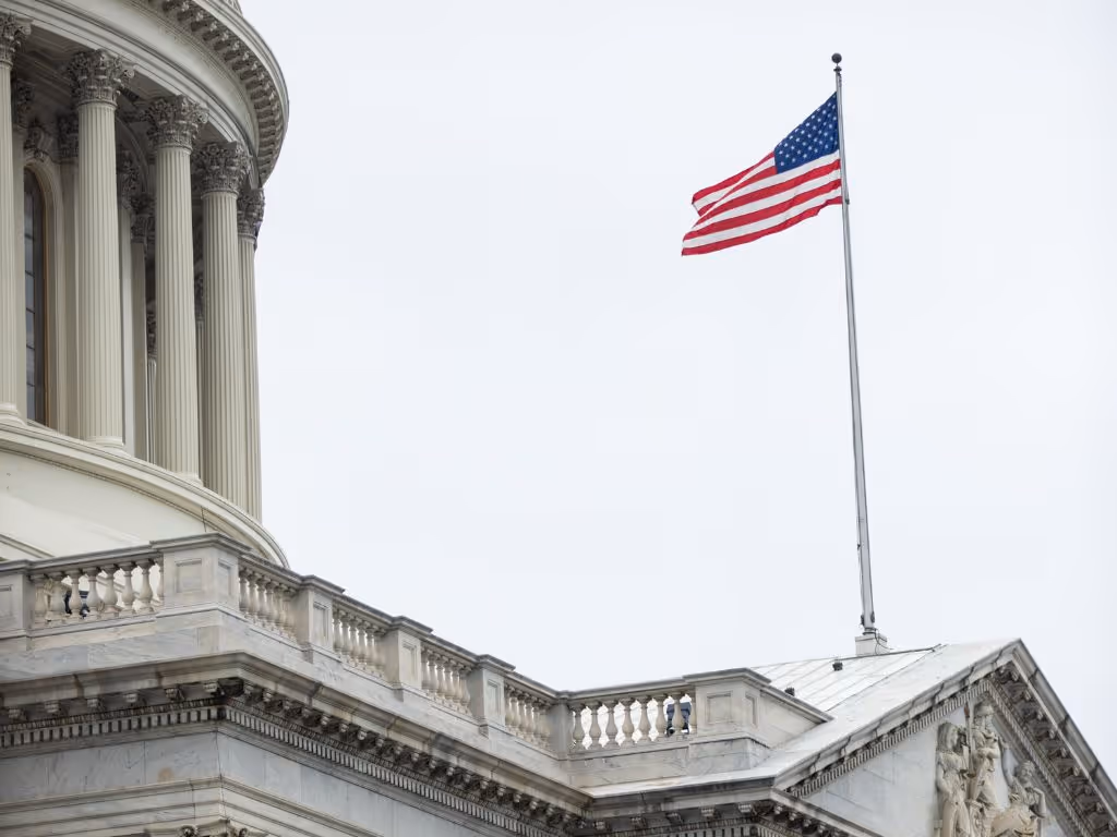 American flag waving net to the dome of the US Capitol building in Washington, D.C.