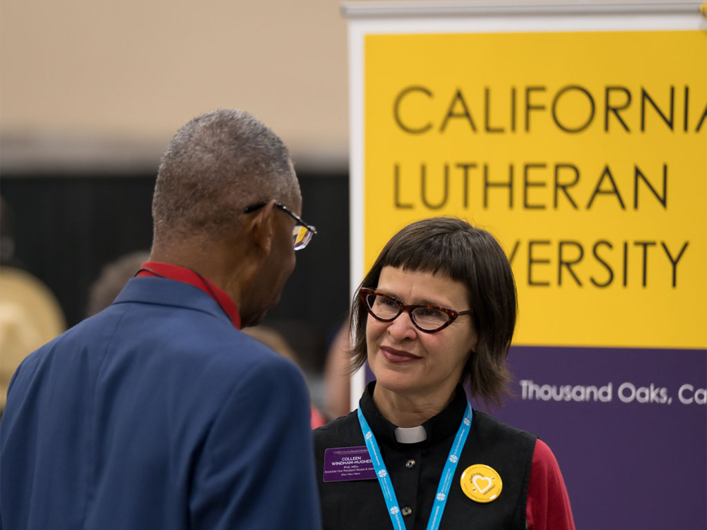 Two people talking at an indoor event with a California Lutheran University sign in the background