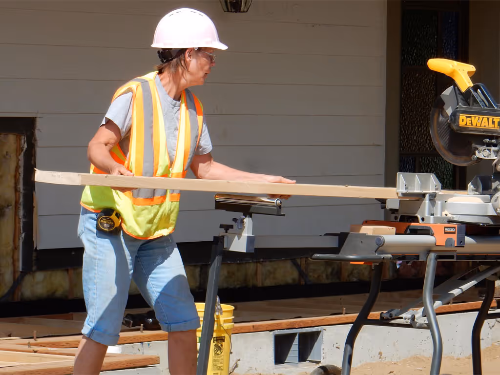 Person wearing a safety vest positioning a wooden board on a power saw outdoors