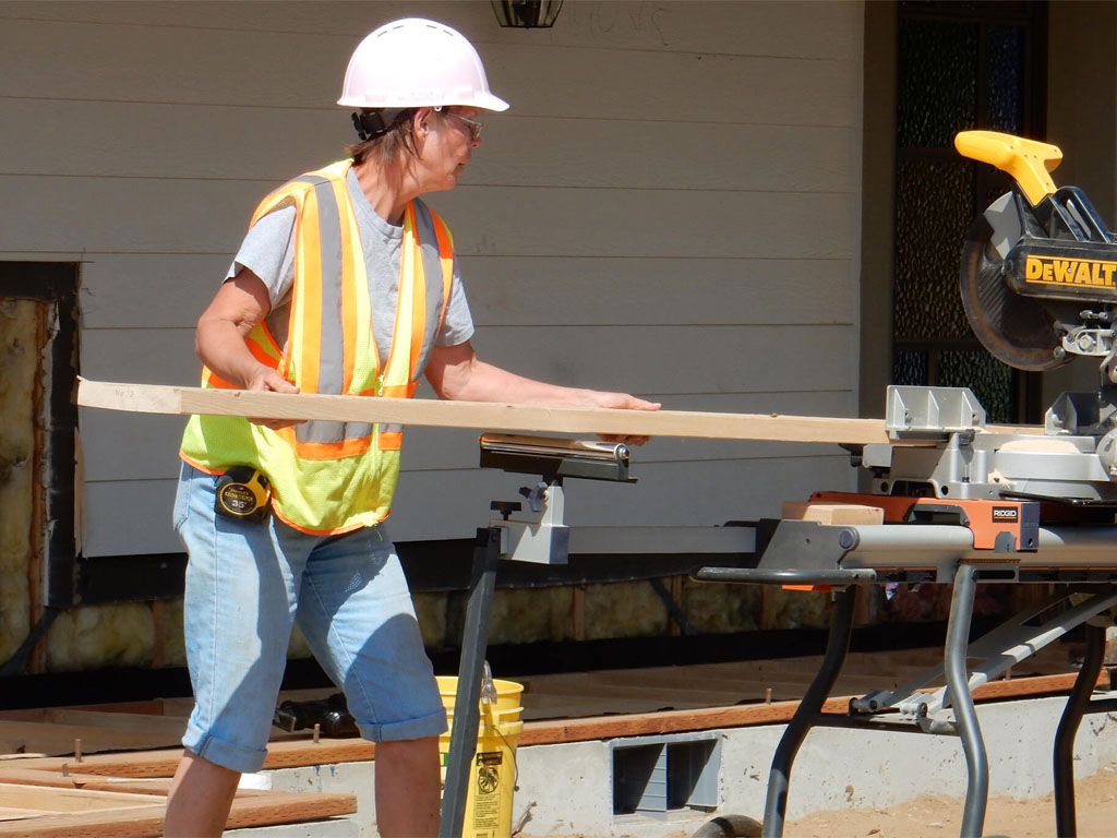 Person wearing a safety vest positioning a wooden board on a power saw outdoors