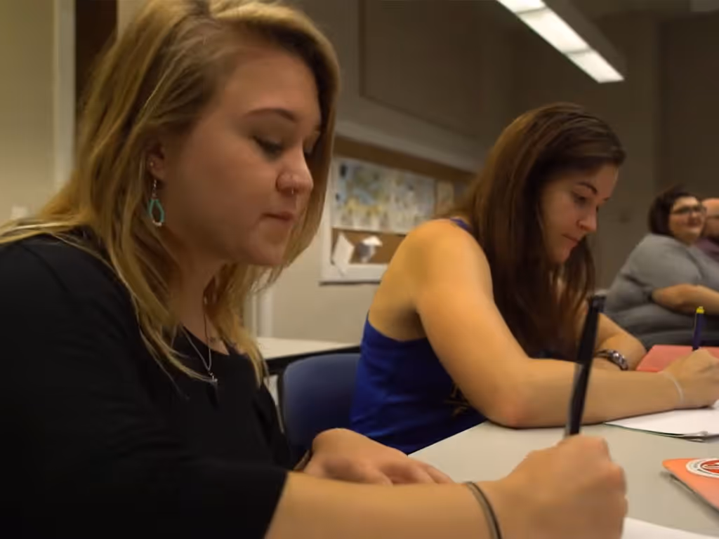 Two adults seated at a table writing on paper during a class