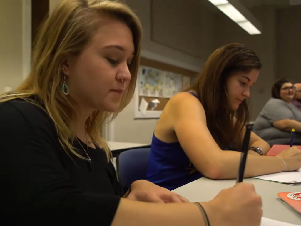 Two adults seated at a table writing on paper during a class