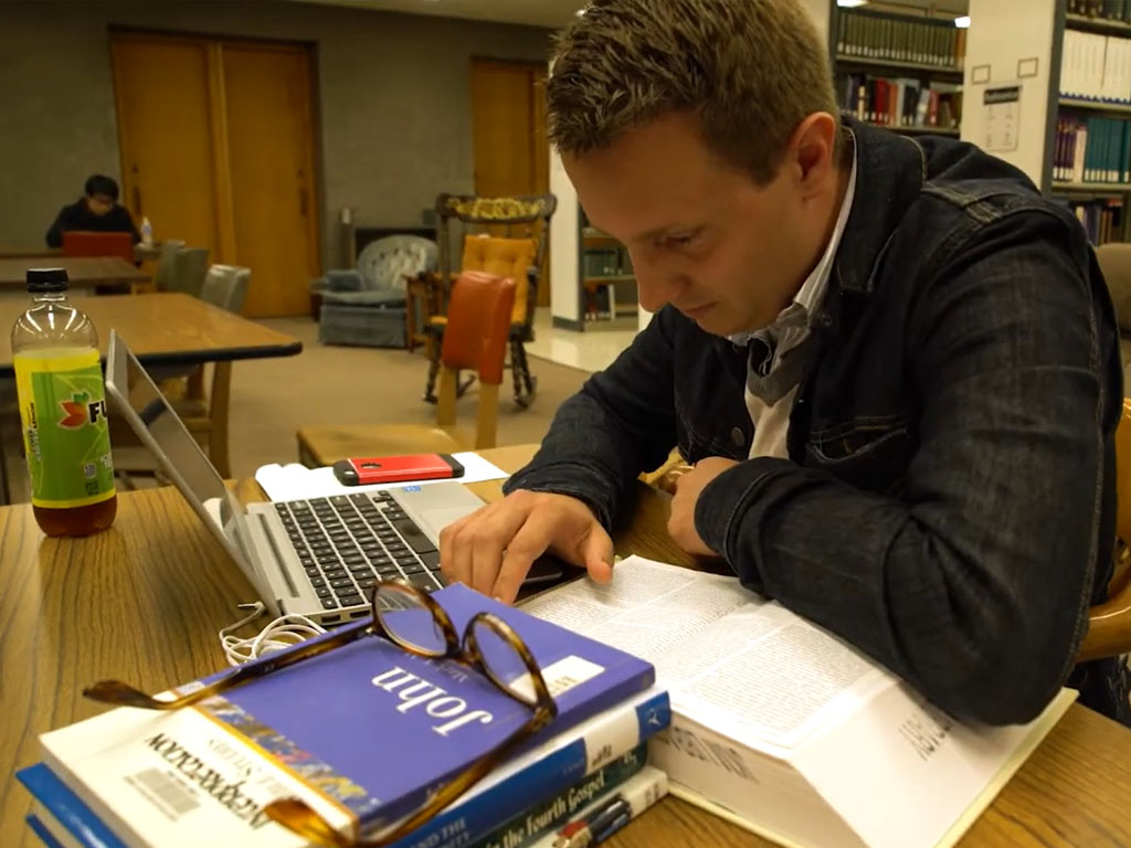 Person working on a laptop at a table with books and papers