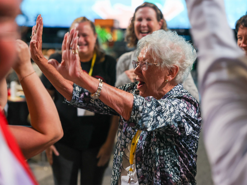 An older woman smiling and raising her hands to high-five another person at an indoor gathering