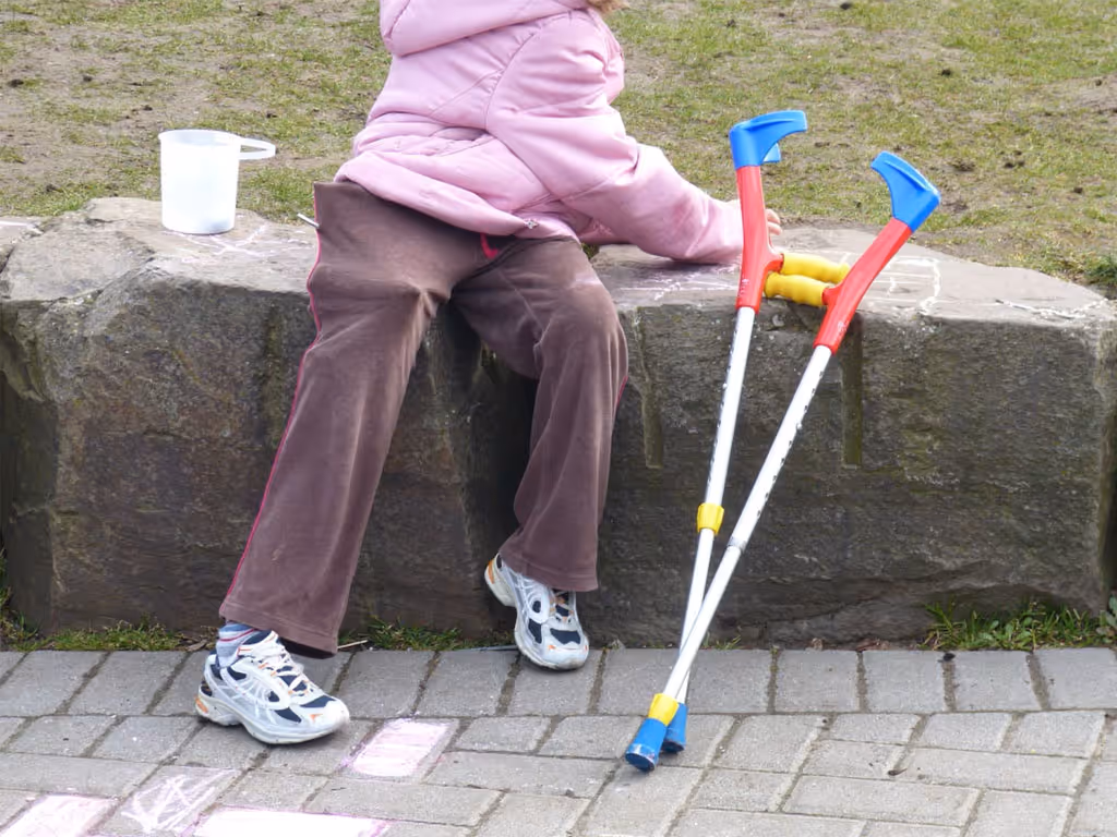 Person seated on a stone ledge outdoors with crutches resting beside them