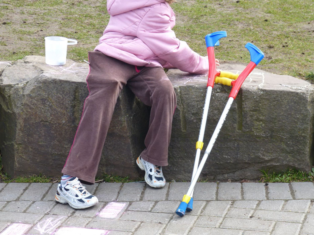 Person seated on a stone ledge outdoors with crutches resting beside them