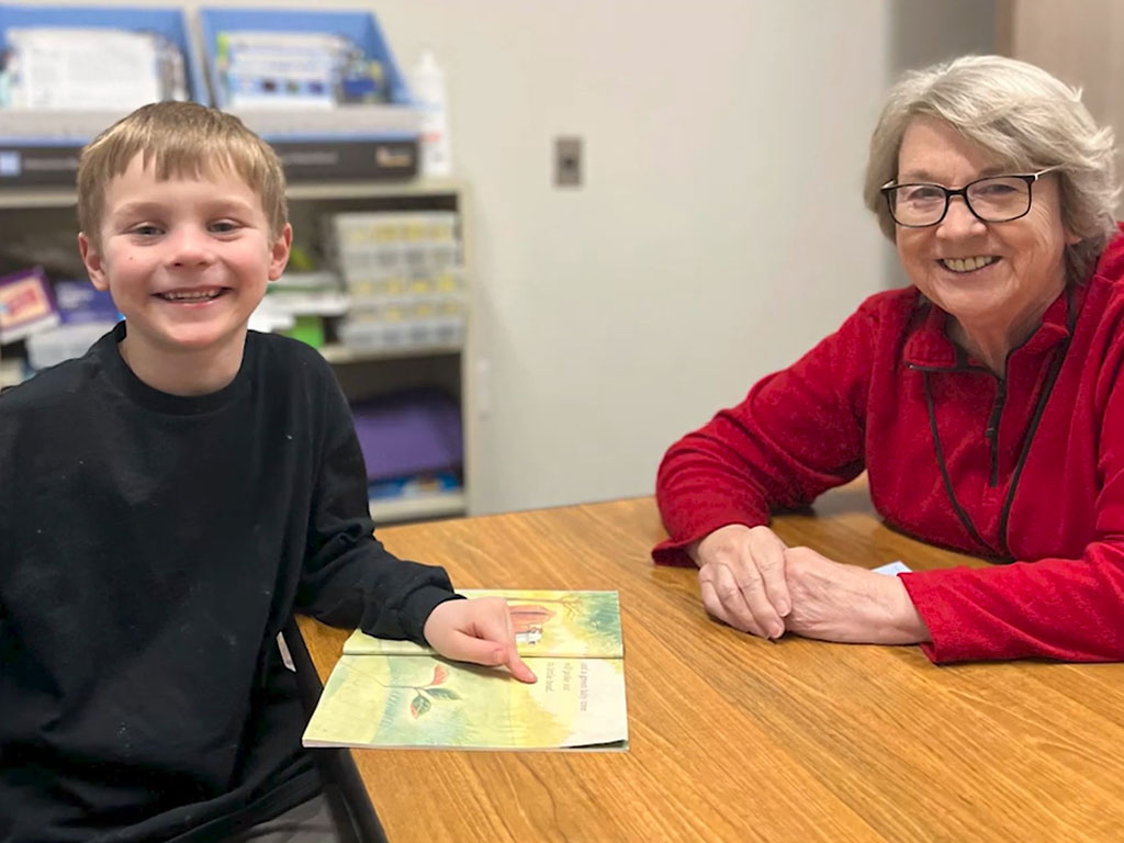 Child and older adult sitting at a table reading together