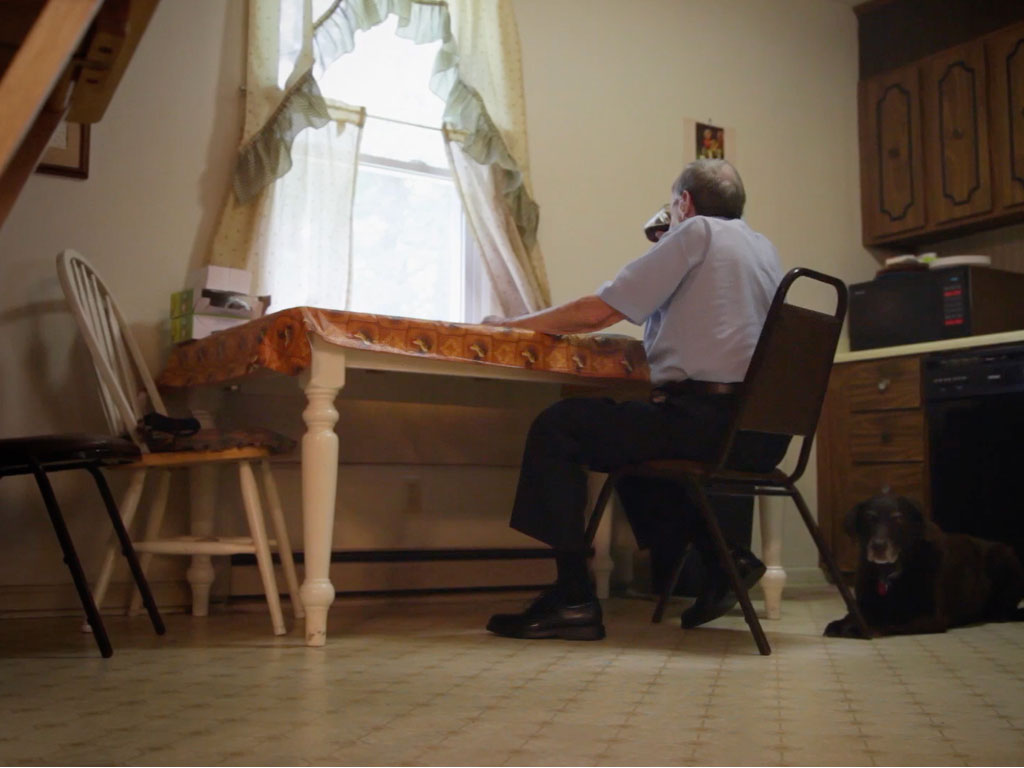 A man sits alone at a table looking out a window while drinking a can of soda.