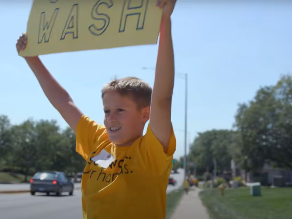Young person outdoors raising their arms while holding a sign