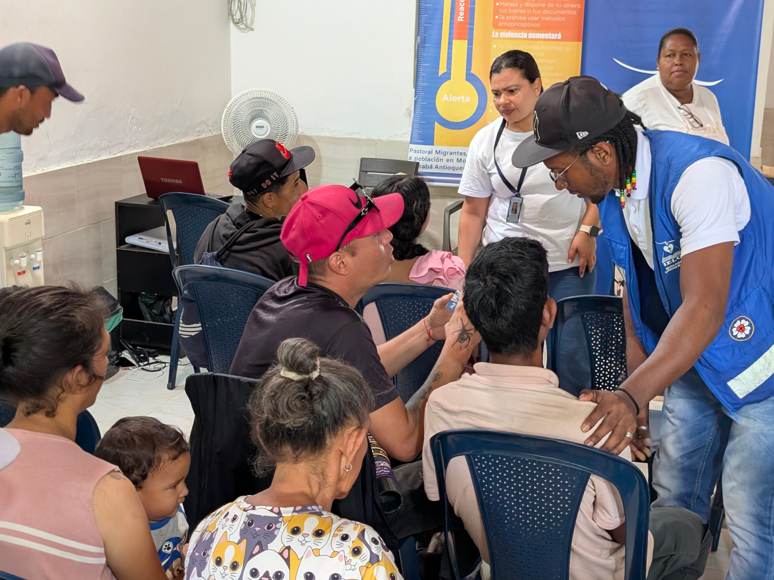 A bald man wearing a suit coat holds a tea light with his left hand as he speaks to a crowd in front of a banner that reads “AMMPARO.”  
