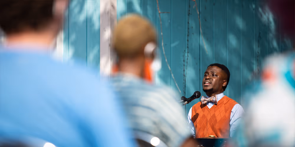 A female with floral shirt and purple vestments with hair in braids holds up her hands to bless the communion bread that sits under a purple cloth on the table. 