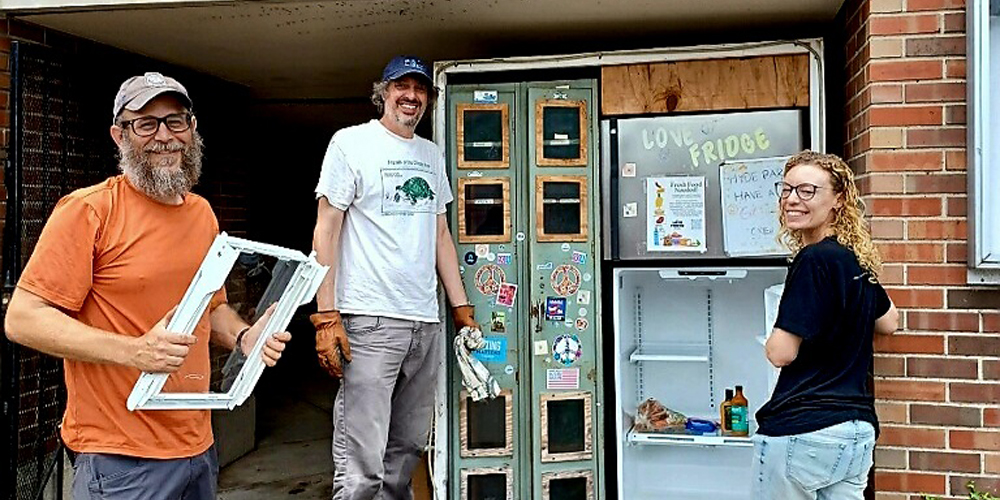 Three people stand in front of a fridge with supplies