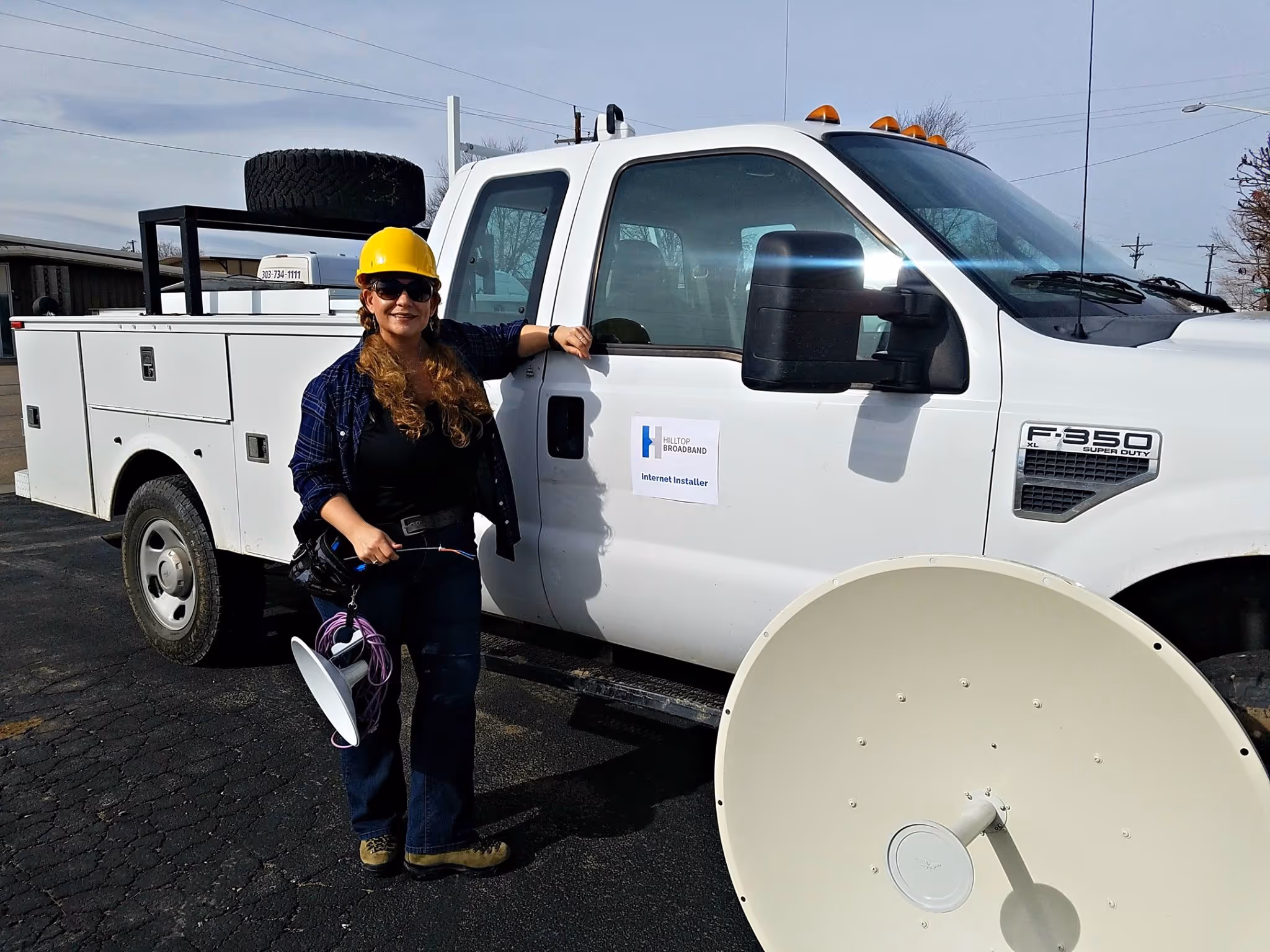 Female Hilltop Broadband technician in hard-hat standing next to work truck.