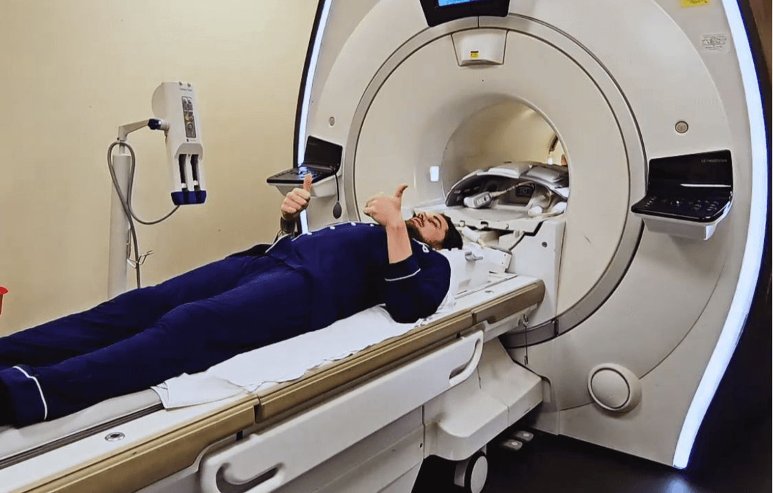 Man giving a thumbs-up while lying inside an MRI machine, preparing for a medical scan.