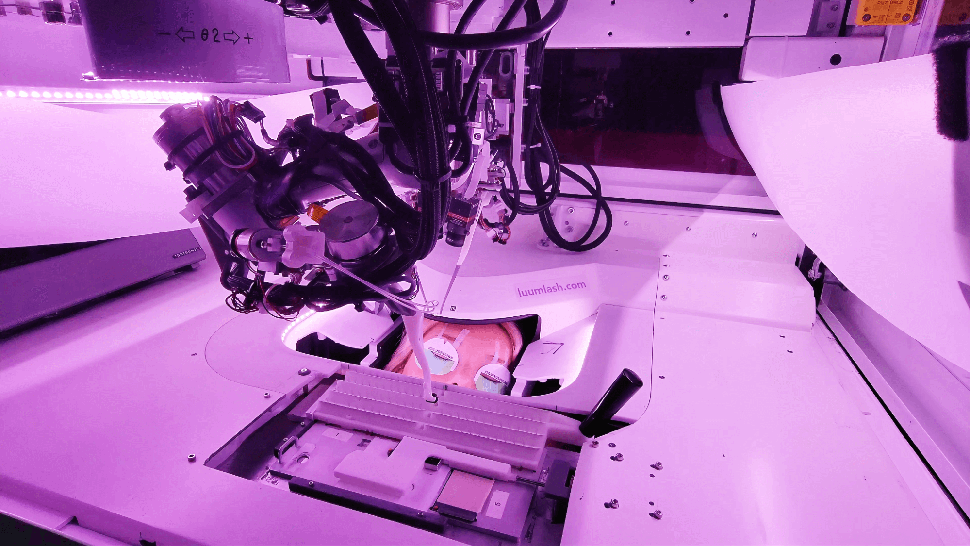 Close-up of high-tech robotic laboratory machine applying eye-lashes with AI samples under purple lighting at LUUM Lash