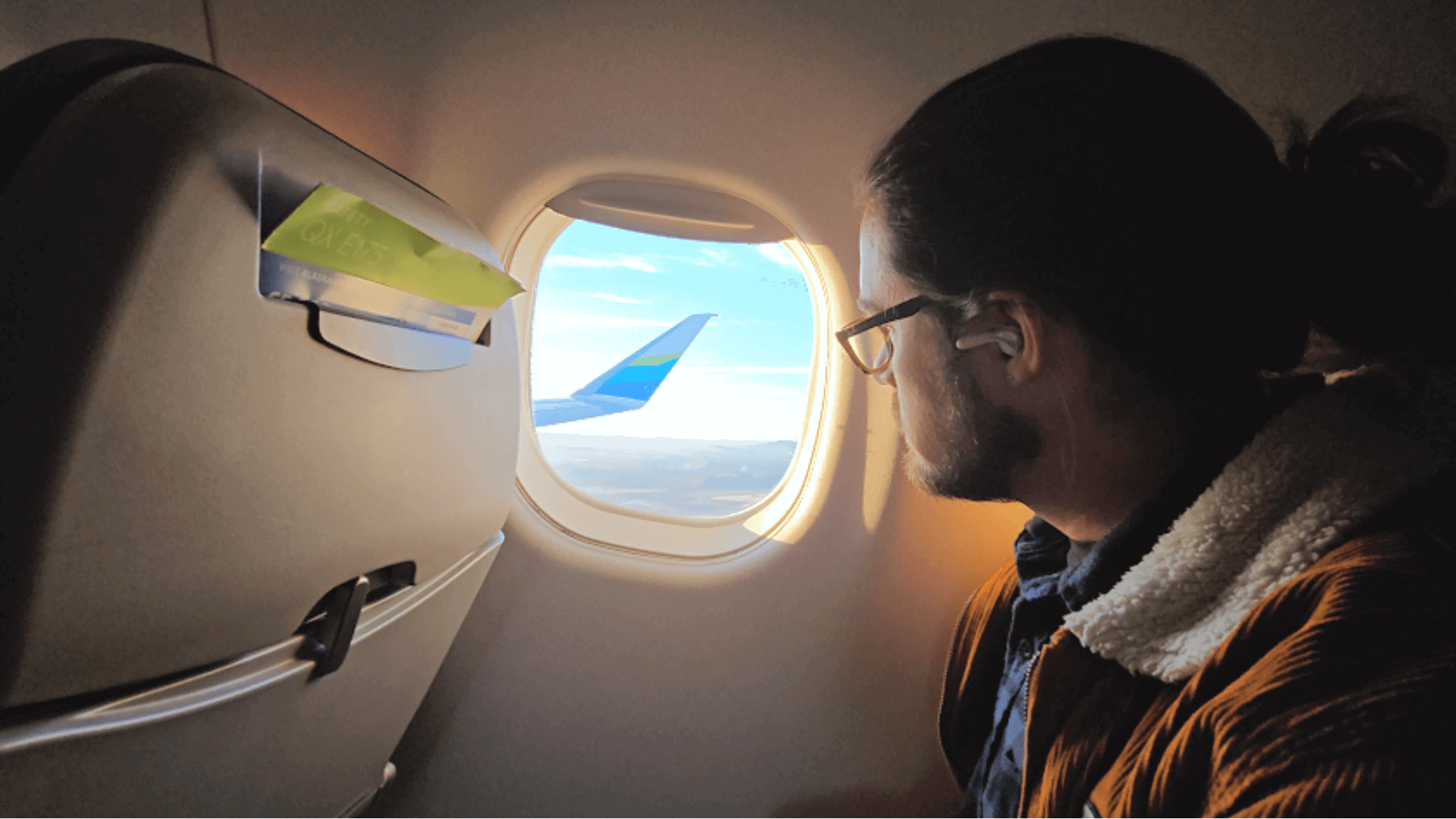 Man looking out airplane window at wing and blue sky during flight from Oregon to California
