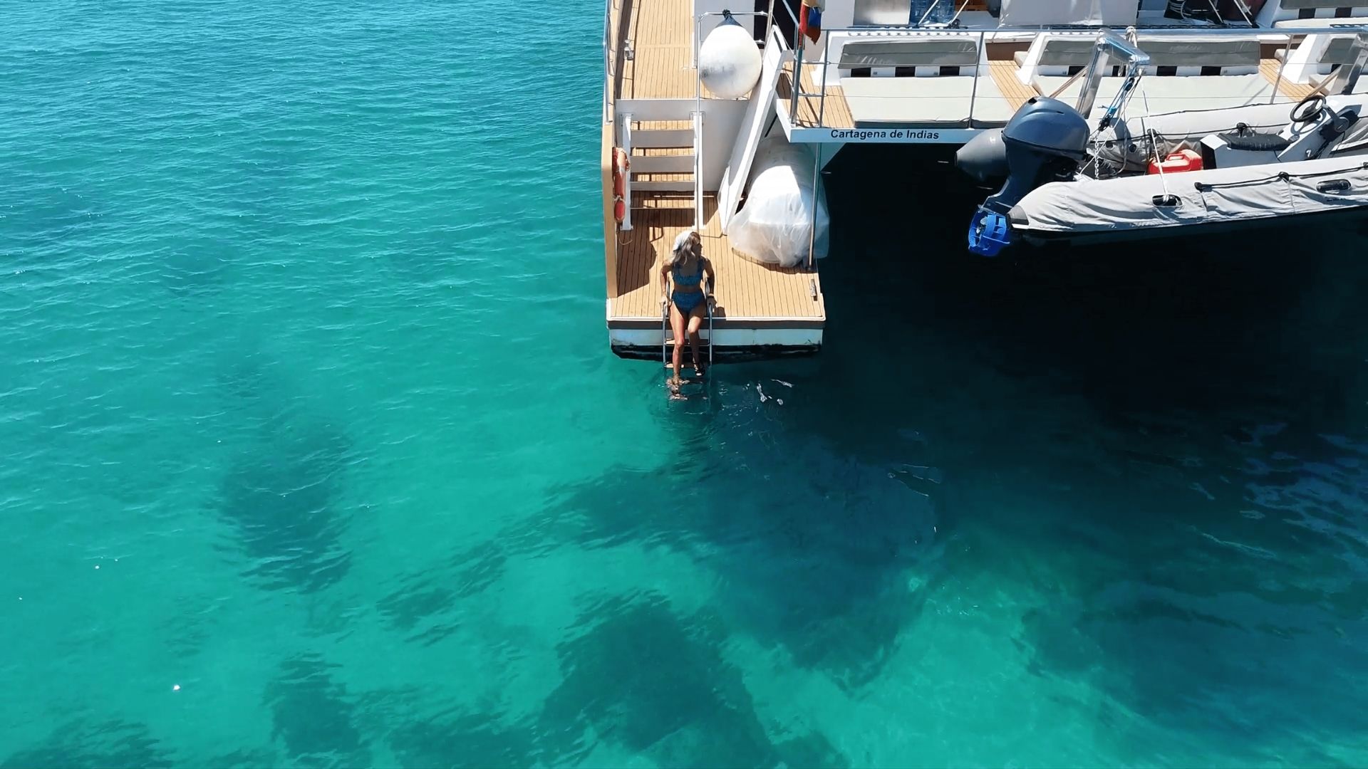  Woman sitting on a catamaran ladder in the turquoise Caribbean waters near Cartagena, Colombia — combining luxury travel with affordable health and beauty tourism.
