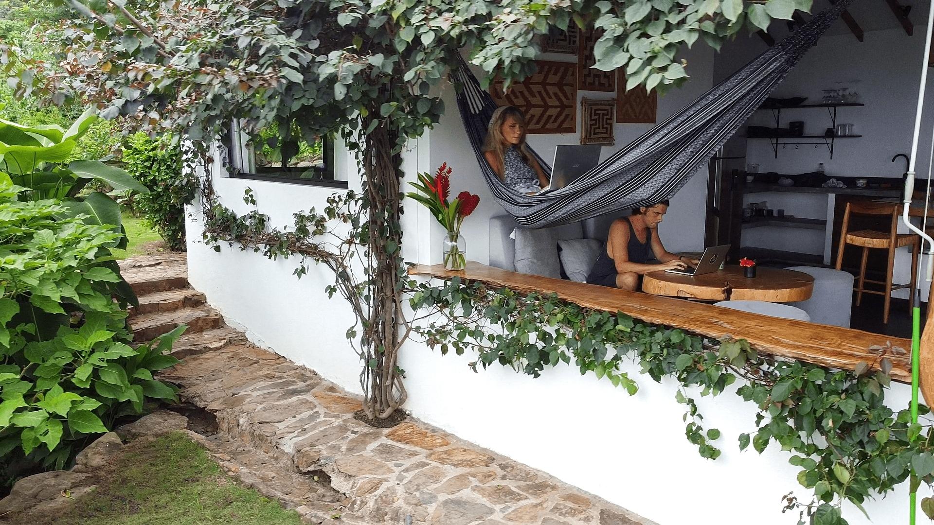 Woman alongside man working remotely from a hammock at a lush eco-retreat in Colombia — combining wellness, nature, and remote work during health and beauty travel.