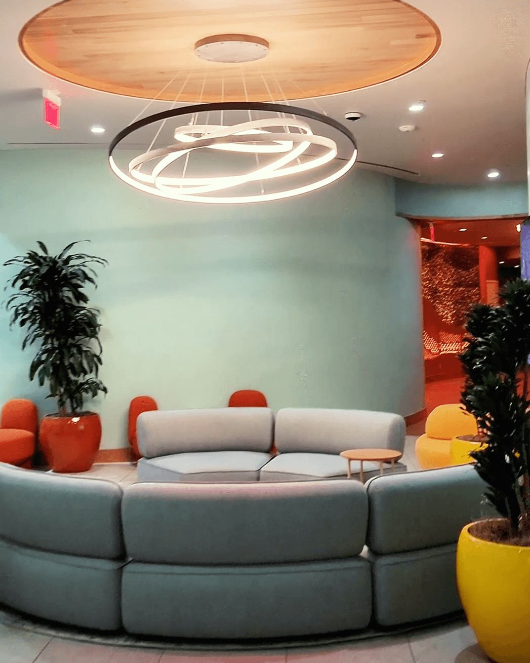 Modern wellness lounge with curved seating, indoor plants, and circular ceiling light fixture