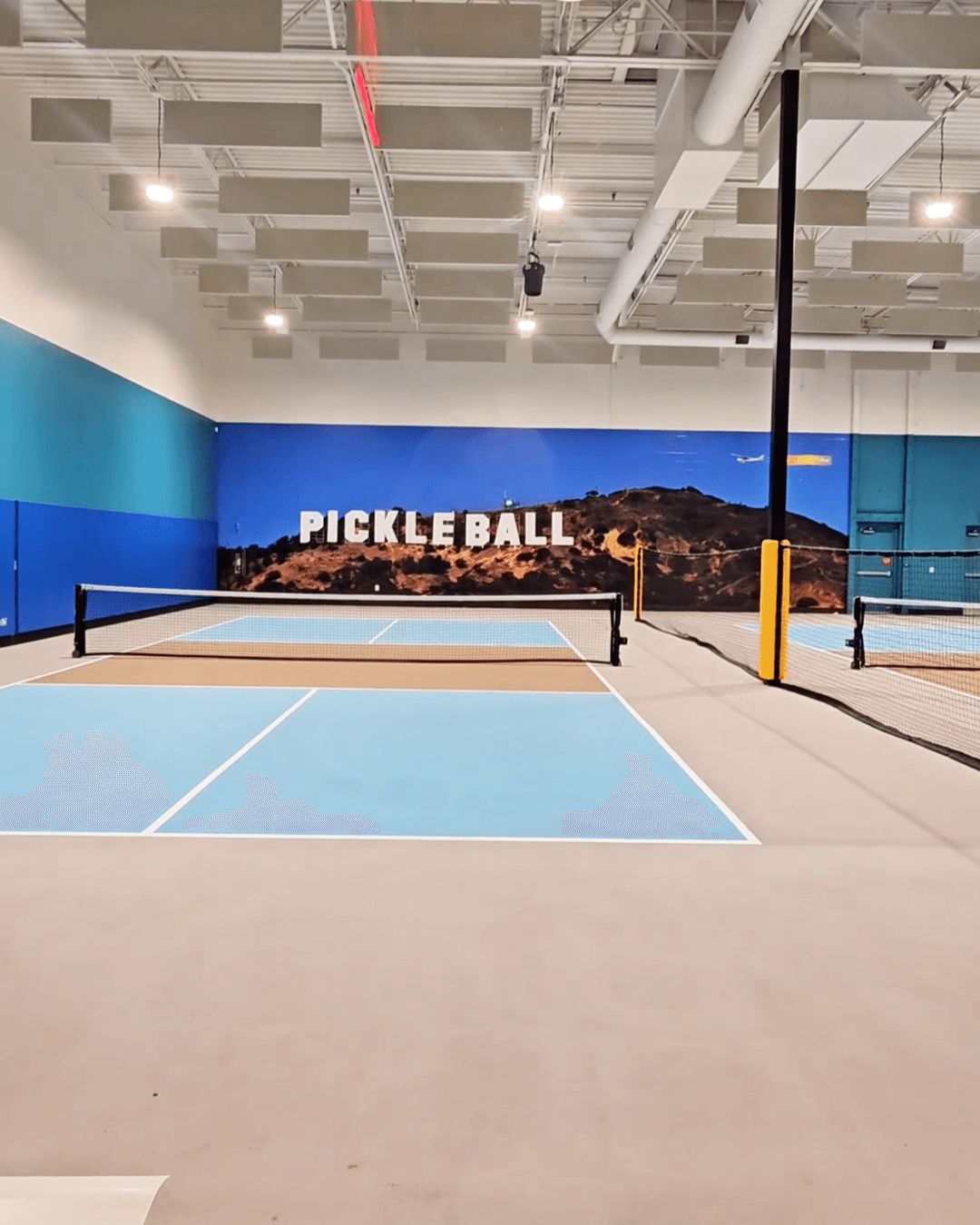 Indoor pickleball court with blue flooring and Los Angeles-themed mural