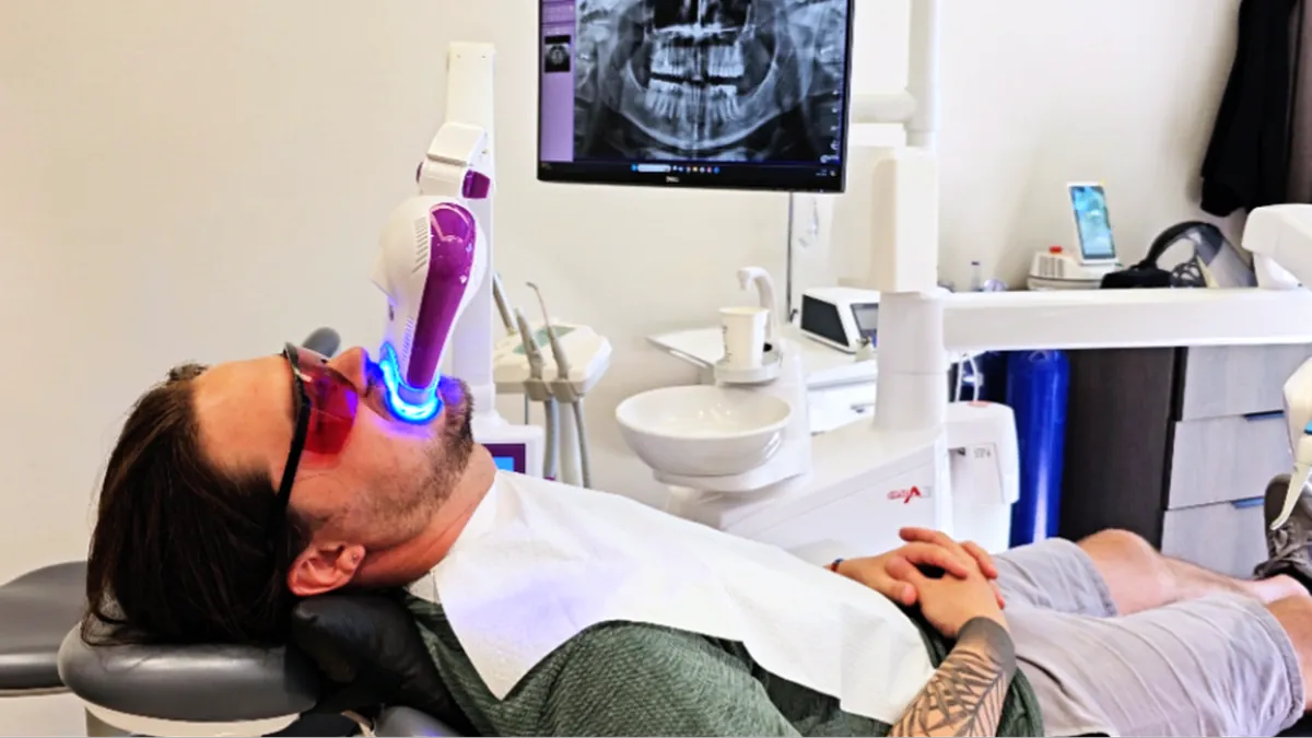 Man receiving teeth whitening with LED light at dental clinic