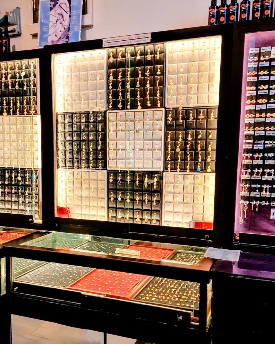Display wall of organized piercing jewelry and trays in lit cabinets