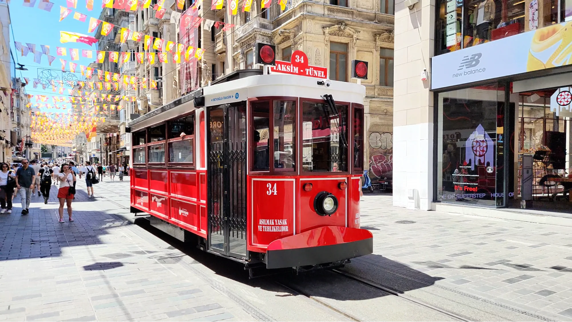 The historic red tram travels down Istiklal Street in Istanbul, surrounded by flags and people shopping.