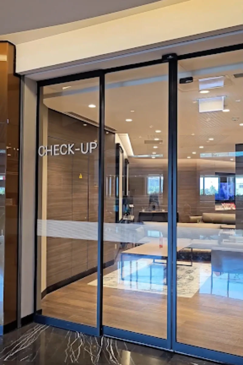 A modern hospital check-up lounge with glass sliding doors, sleek interiors, and a comfortable seating area visible inside.