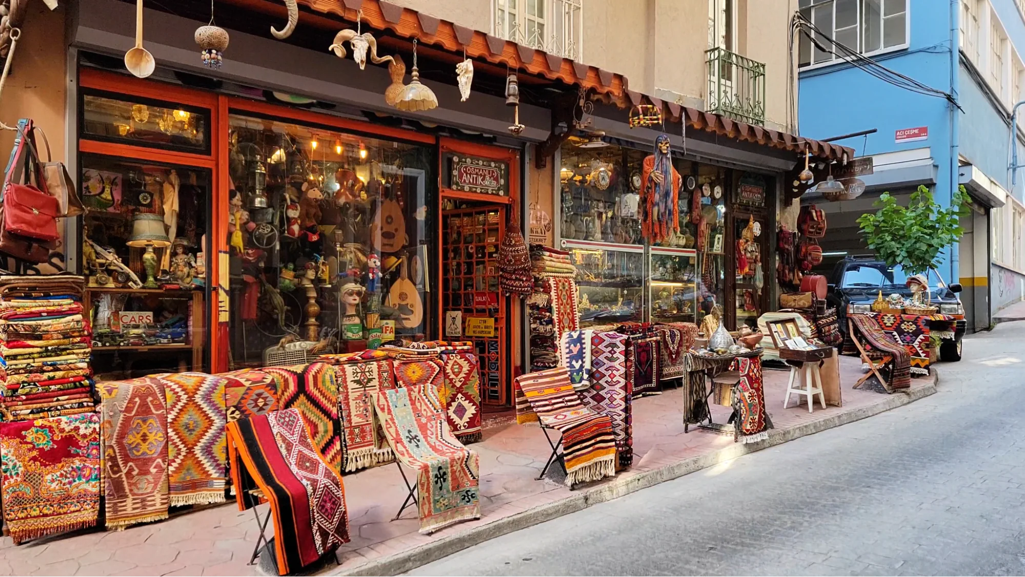 Colorful Turkish rugs are displayed outside a packed antique store in Istanbul with hanging lamps, instruments, and traditional crafts.