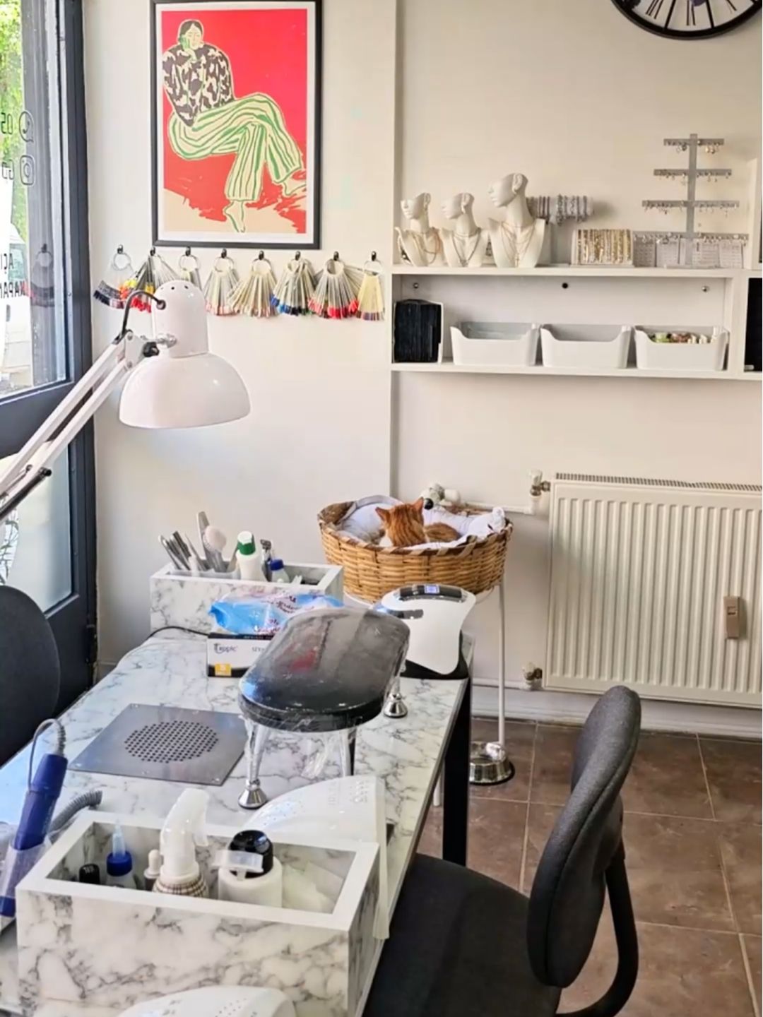 A cozy nail salon interior in Istanbul with a marble worktable, manicure tools, wall art, and a cat resting in a basket.