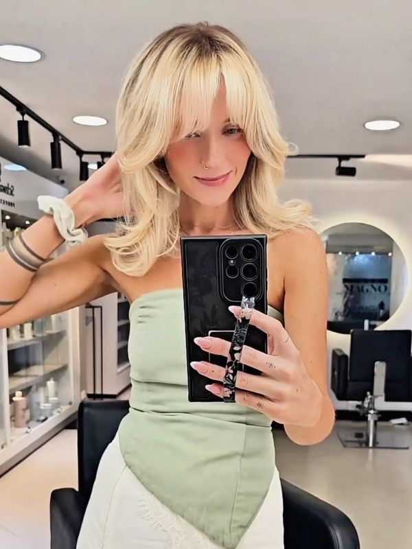 A blonde woman poses confidently after a hair makeover in a white and green outfit at Casa Magno.