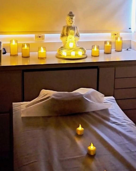 A spa bed surrounded by LED candles and a Buddha statue sits in a dimly lit wellness room.
