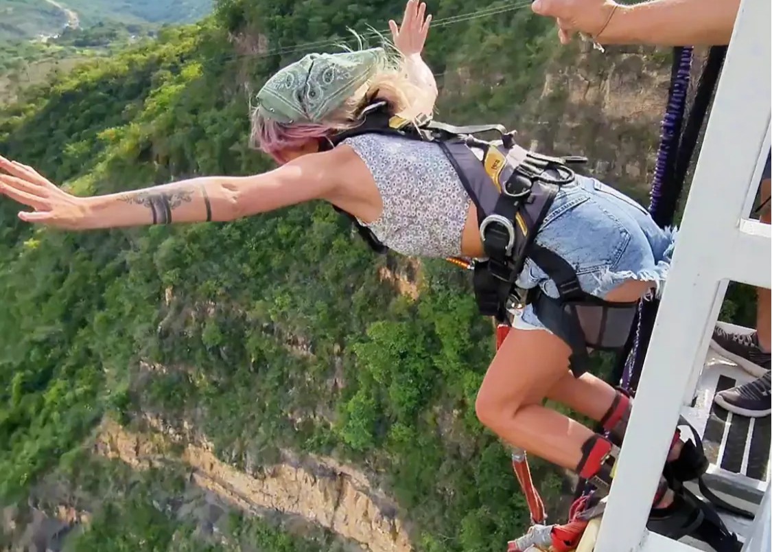 A woman leaps off a high platform for a bungee jump over a lush canyon in Colombia, arms outstretched mid-air.