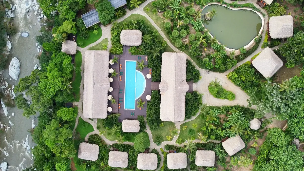 Aerial view of eco-resort in Colombia with thatched-roof bungalows, swimming pool, and surrounding jungle