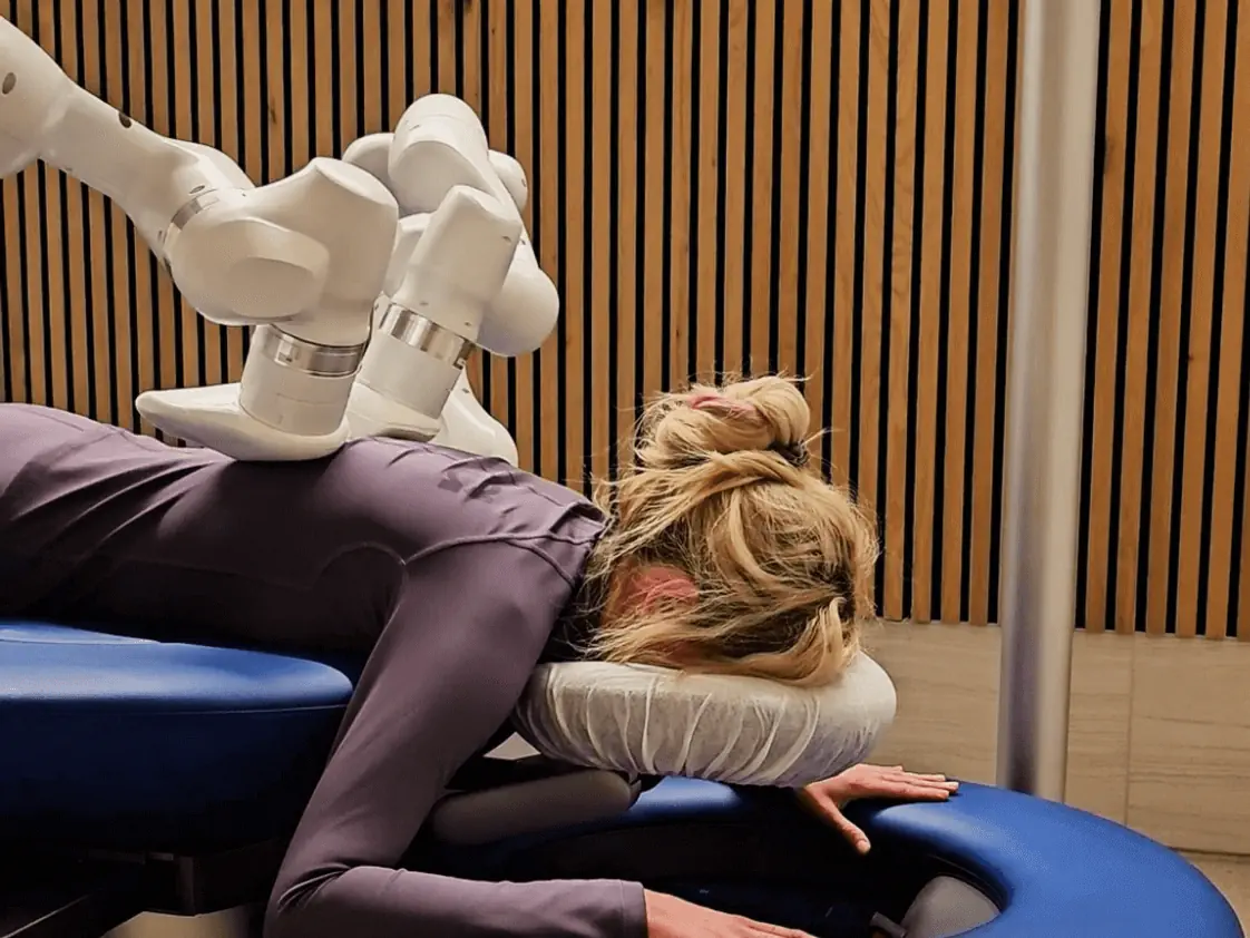 A woman receiving a massage from a futuristic robotic massage system in California, lying face down on a blue massage bed.  