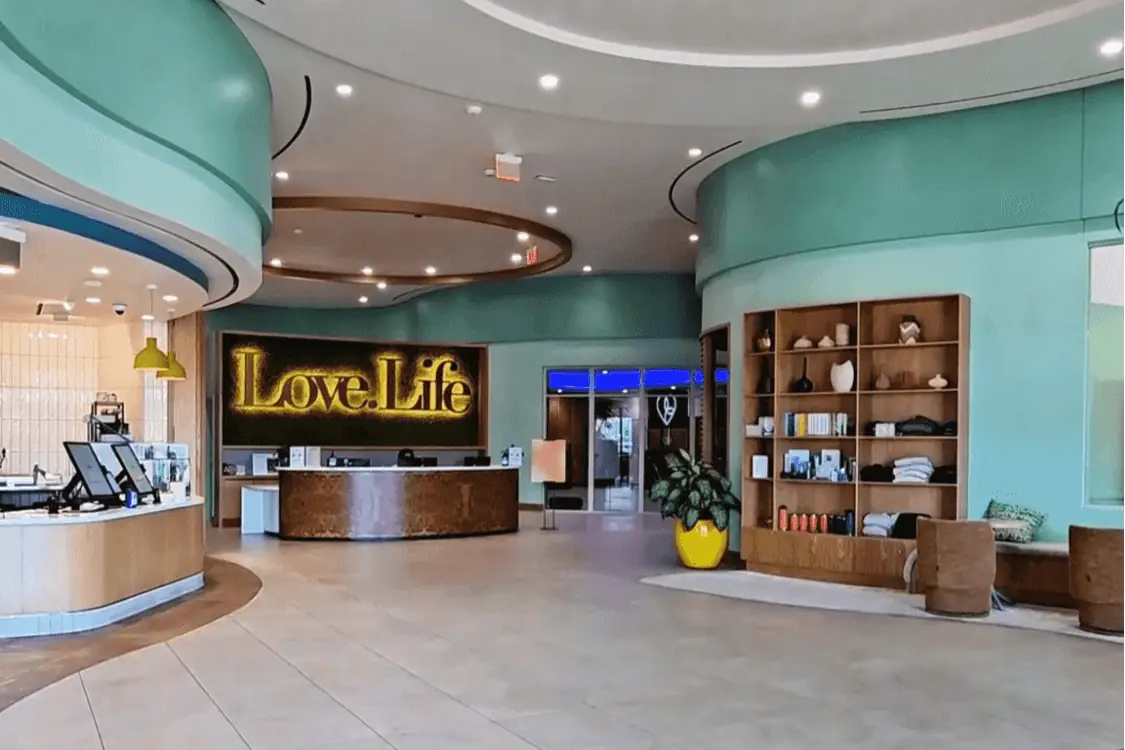 The bright and modern lobby of Love Life Health and Longevity Center in California, featuring a reception desk, boutique shelving, and a glowing “Love.Life” sign.  
