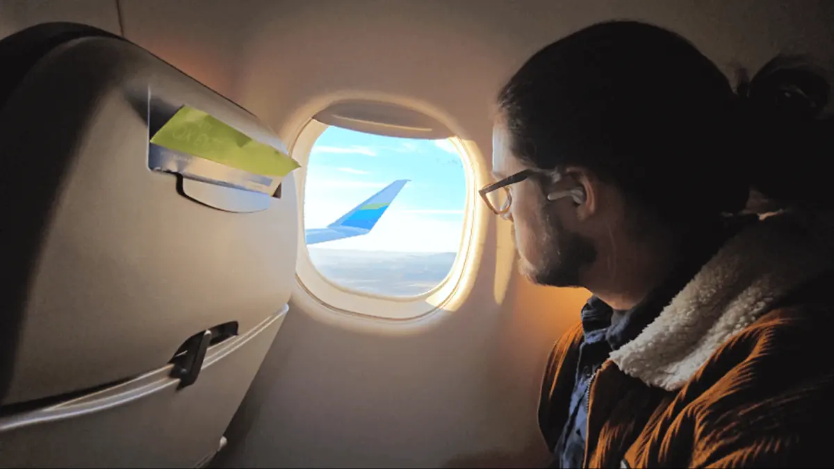A passenger looking out the airplane window at the wing and sky while flying into California.  