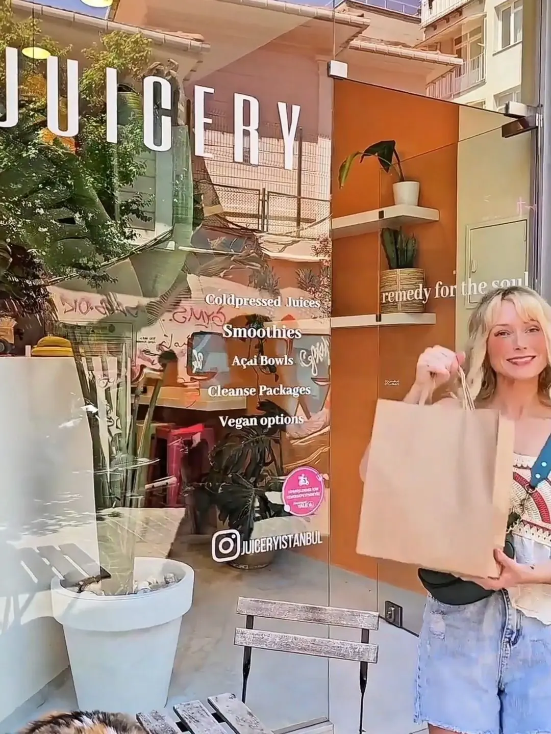 Woman holding a paper bag outside Juicery Istanbul, a modern juice bar offering cold-pressed juices, smoothies, cleanse packages, and vegan options.