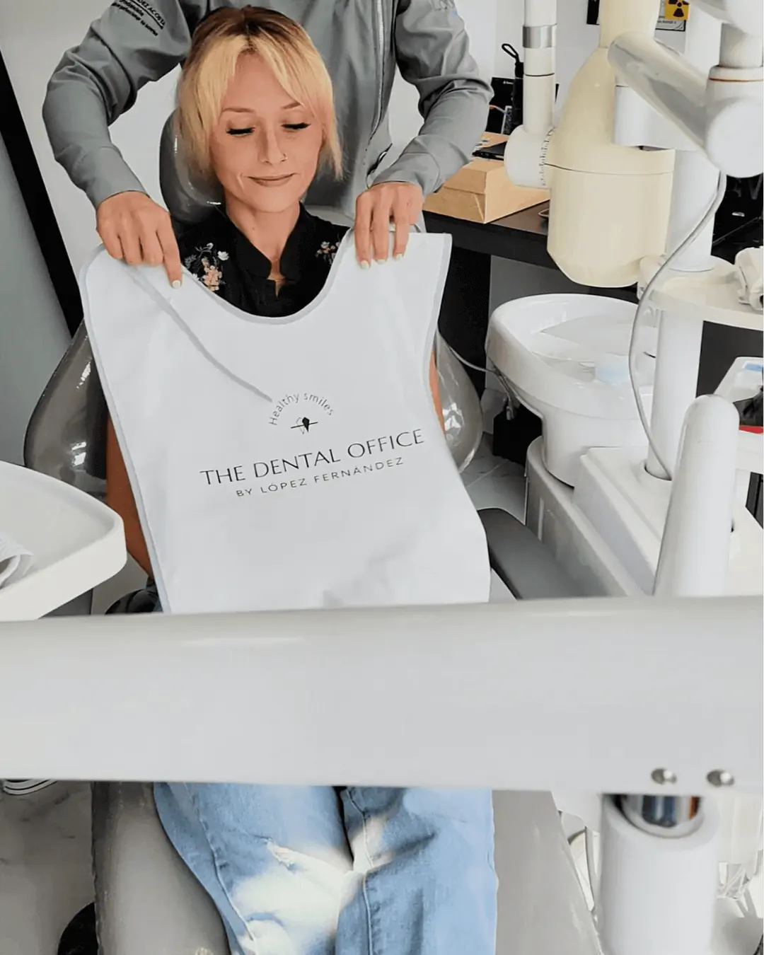A patient at The Dental Office in Medellín, Colombia, being prepared for treatment with a protective bib applied by a dentist.