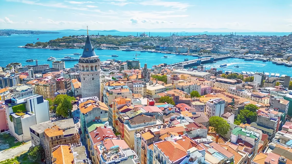 Aerial view of Istanbul featuring the historic Galata Tower, colorful rooftops, and the Bosphorus Strait with boats, showcasing Turkey’s cultural and scenic beauty.  