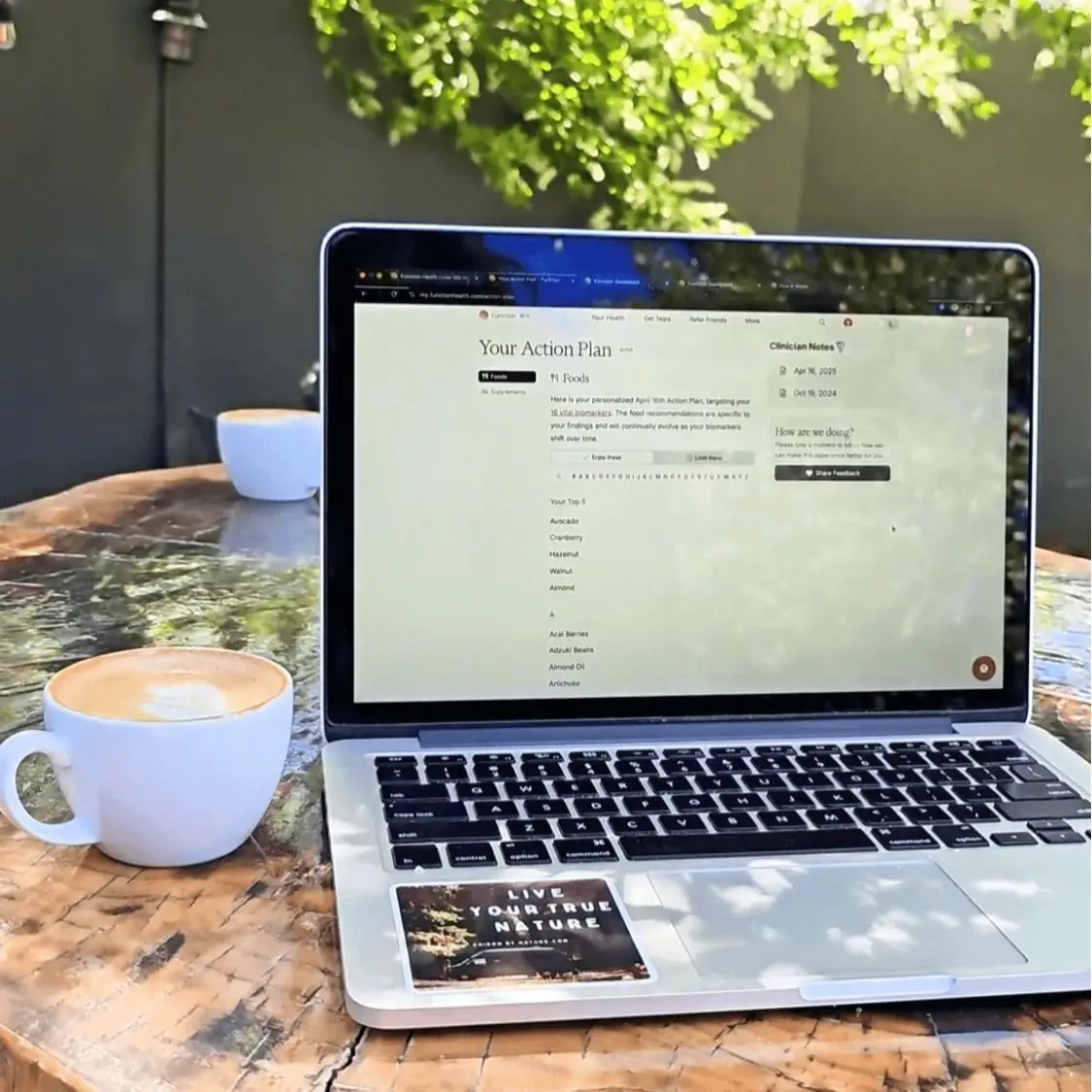 Laptop on an outdoor table displaying a personalized health action plan with recommended foods like avocado, cranberry, hazelnut, walnut, and almond, next to a cup of coffee.