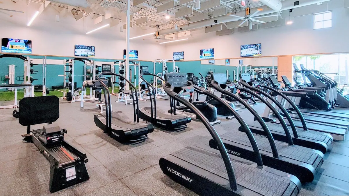 Spacious gym at Love.Life featuring treadmills, weightlifting equipment, and large TVs